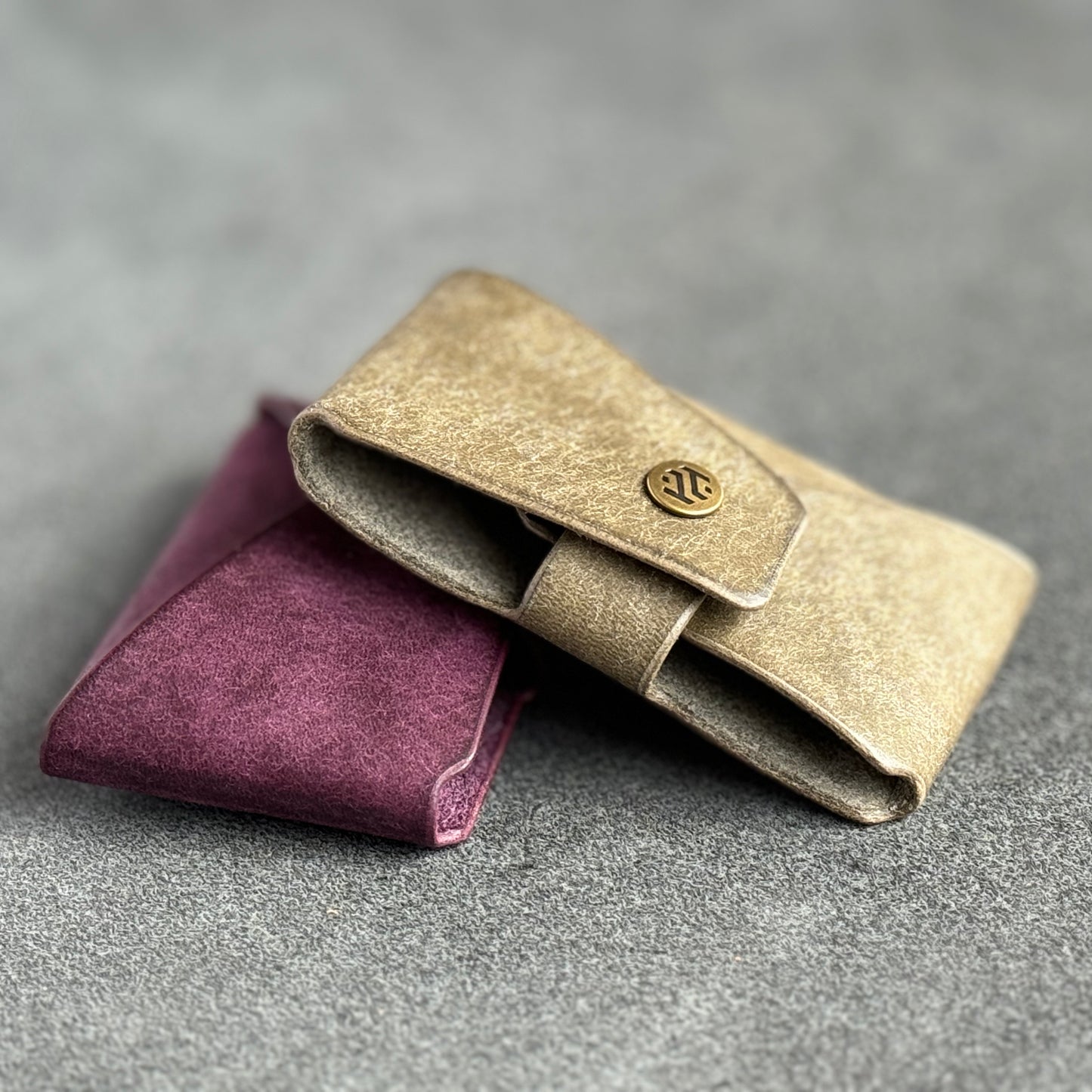 Two minimalist leather wallets, one in light beige and the other in deep purple, displayed on a gray surface.