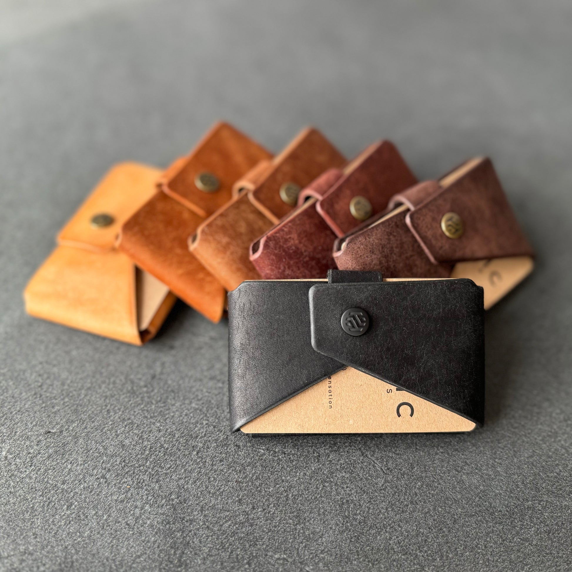 Six minimalist leather wallets in various shades arranged on a flat surface, showcasing the variety of colors available.